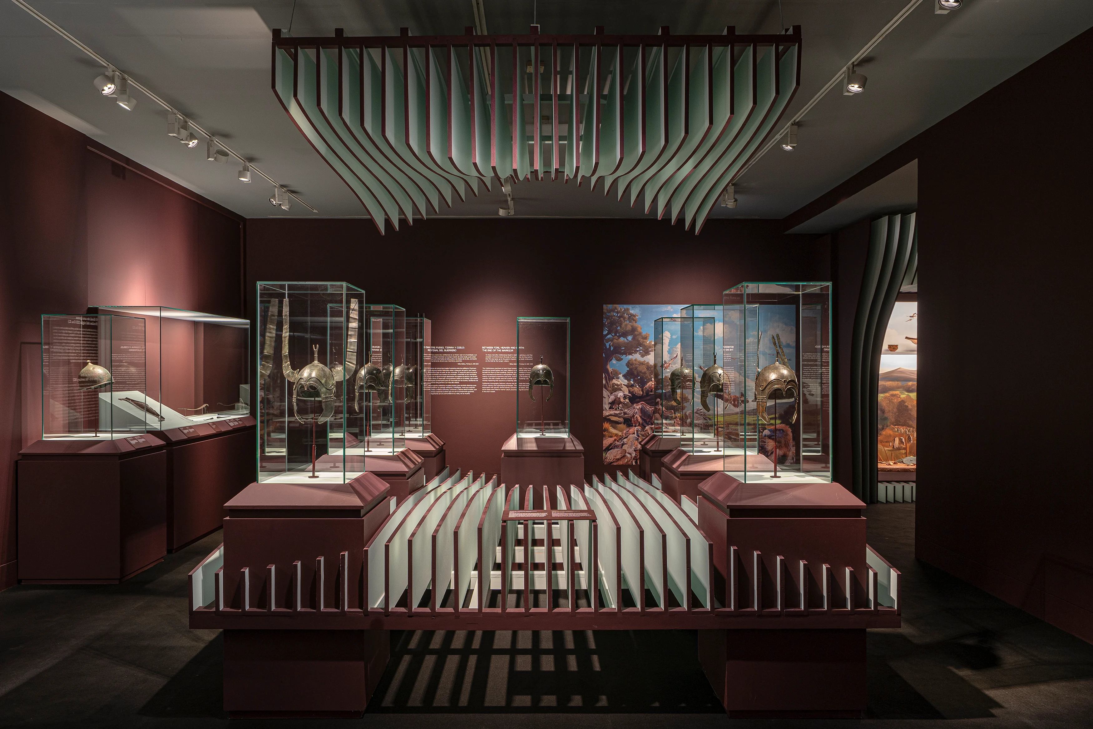 Sala de Alas para la Guerra en el Museo Arqueológico Nacional, con vitrinas y gráfica en tonos burdeos